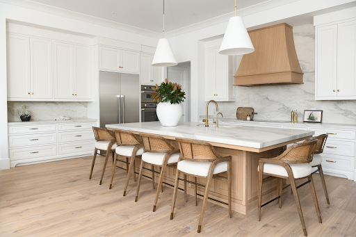 Large kitchen island with light marble top, dark cabinets, gold handles, cake stand, and tall vase.